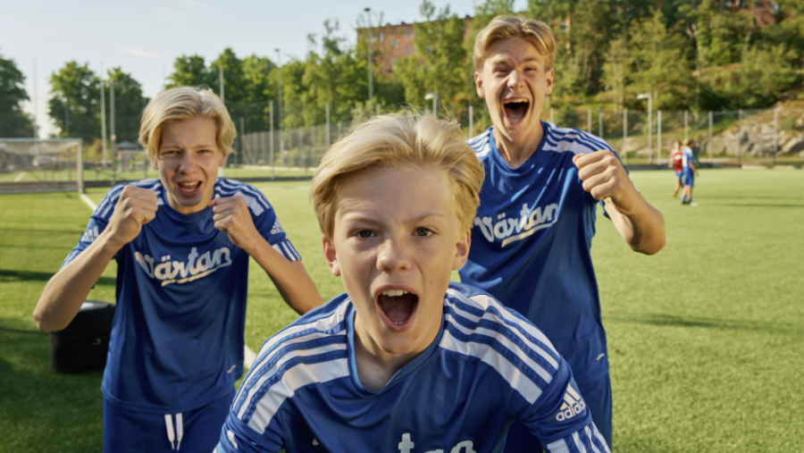 Tre killar jublar på fotbollsplan.